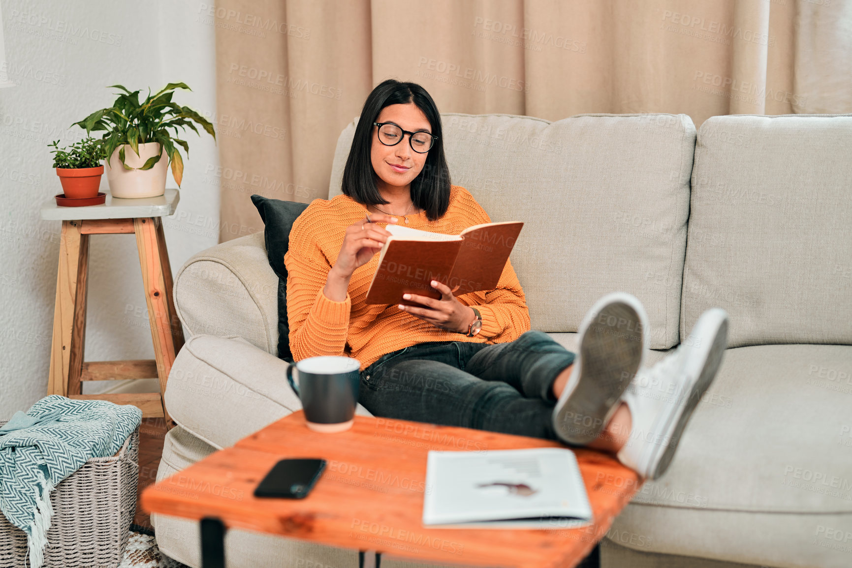 Buy stock photo Shot of a young reading a book while working on the sofa at home