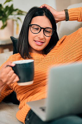 Buy stock photo Shot of a young woman using a laptop and having coffee on the sofa at home