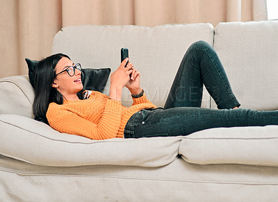 Buy stock photo Woman, smartphone and relax on couch with smile for text, social media and glasses in living room. Chatting, happy and laying on sofa at home for rest, networking and browsing online in lounge