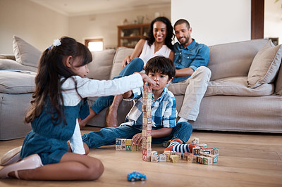 Buy stock photo Shot of two young siblings playing with their toys while their parents sit and watch in the background