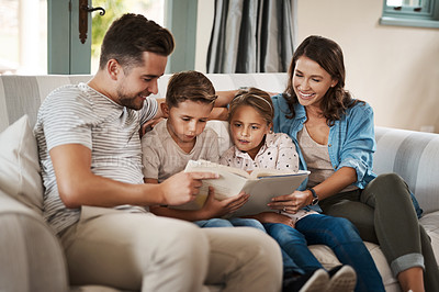 Buy stock photo Shot of a young family of four reading a book together on the sofa at home
