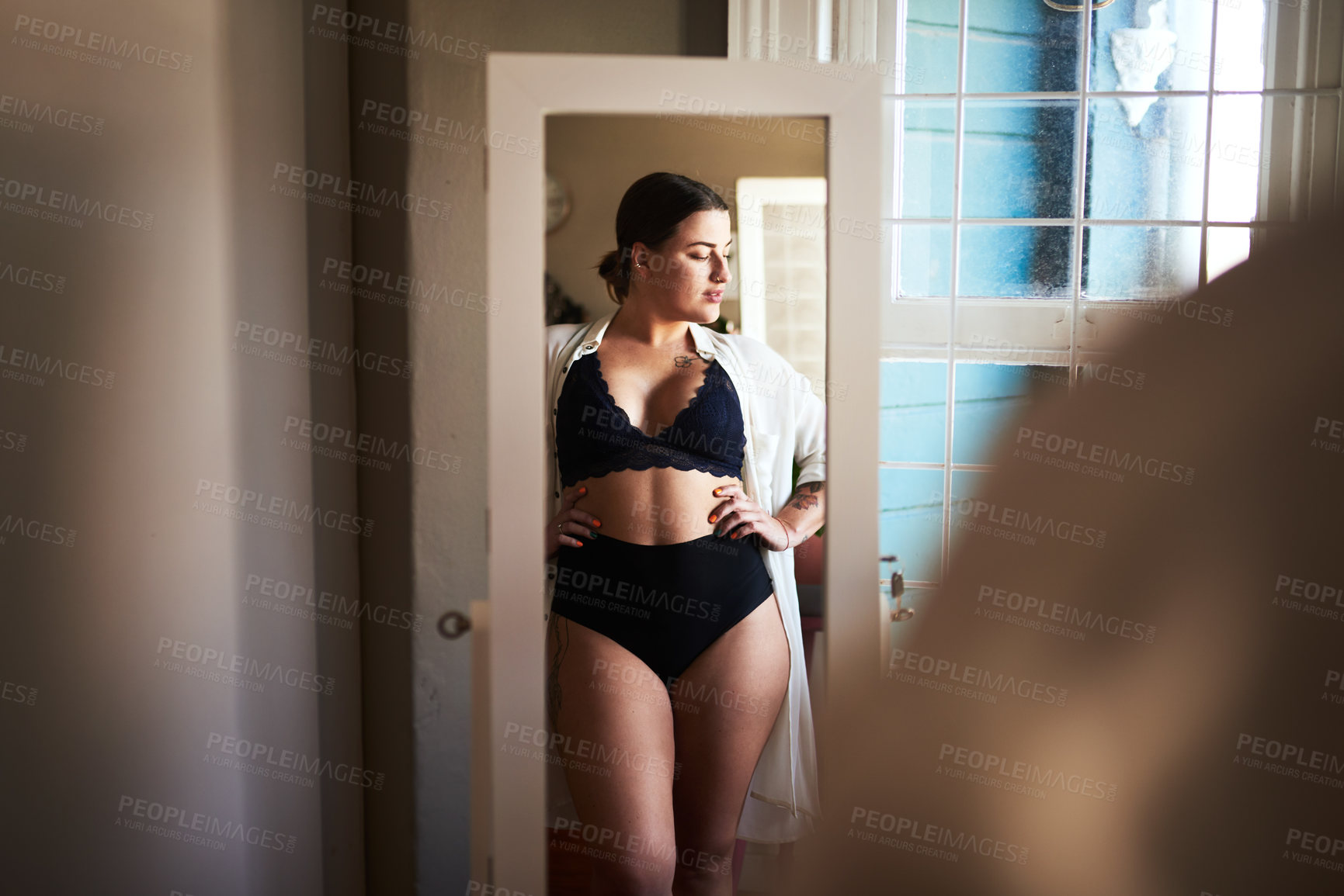 Buy stock photo Cropped shot of an attractive young woman admiring herself in the mirror in her bedroom at home
