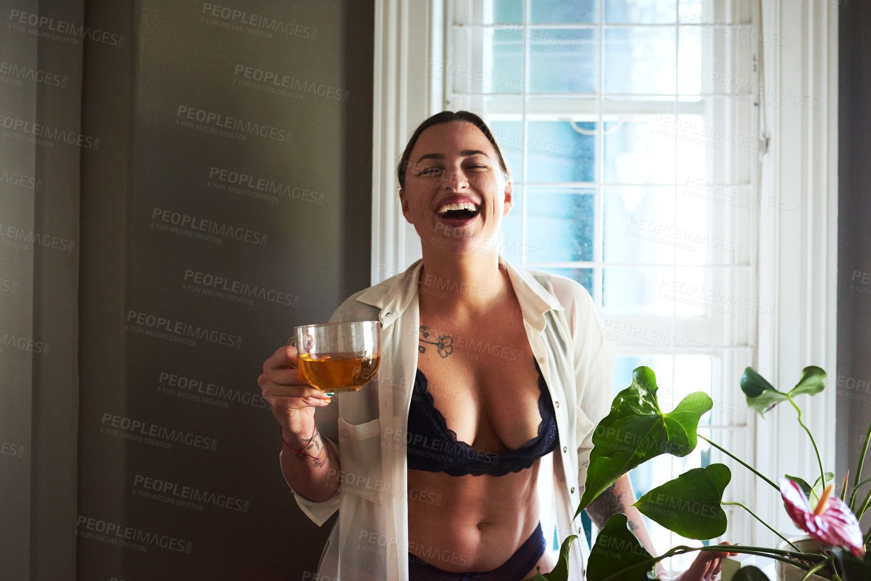 Buy stock photo Cropped shot of an attractive young woman laughing while holding a glass of tea in the morning at home