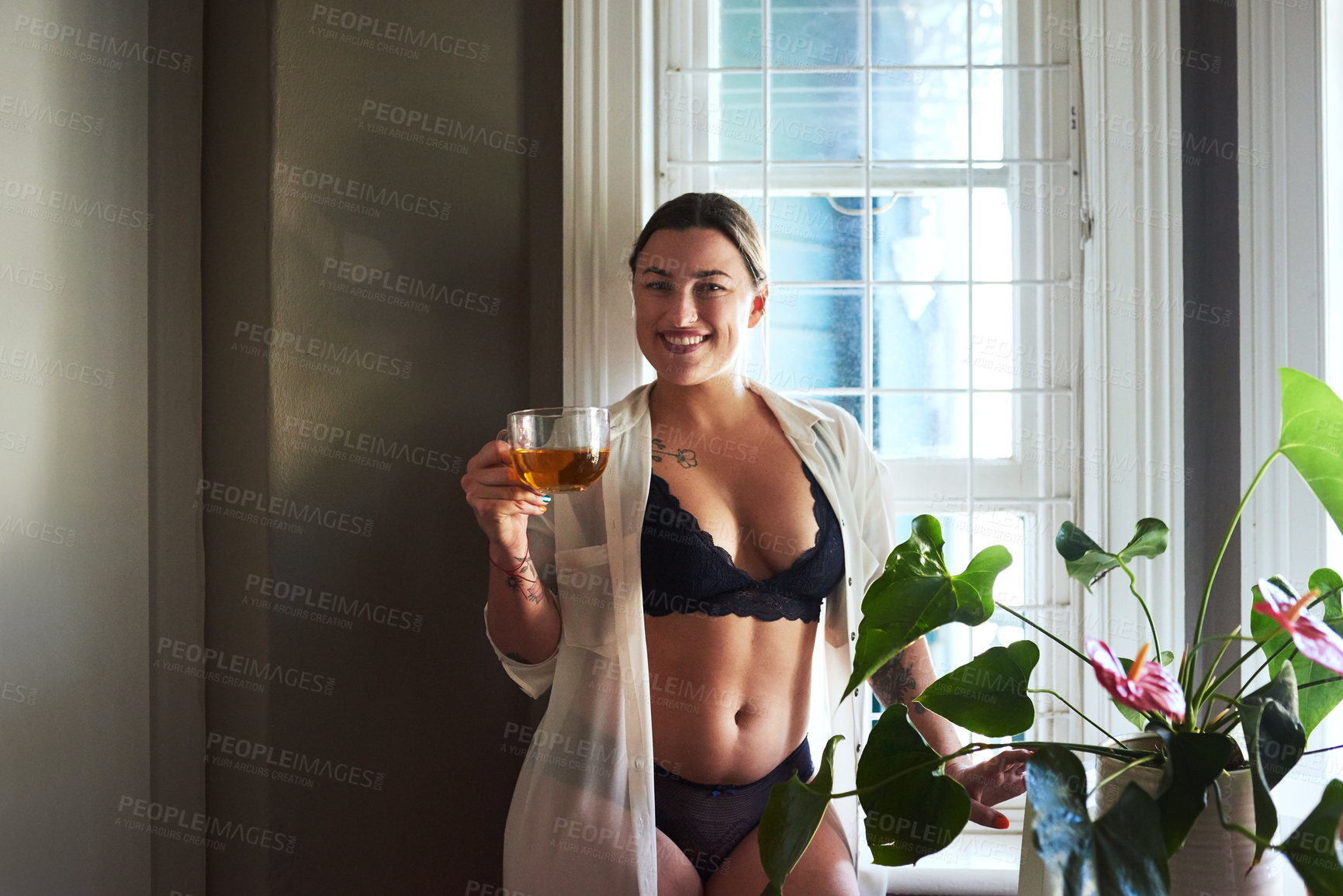 Buy stock photo Cropped portrait of an attractive young woman smiling while holding a glass of tea in the morning at home