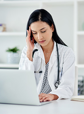 Buy stock photo Shot of a young doctor looking stressed while using a laptop at her desk