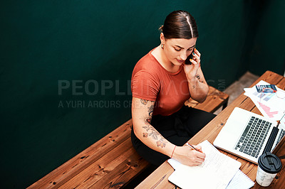 Buy stock photo Cropped shot of an attractive young businesswoman sitting alone and using her cellphone while writing in her notebook