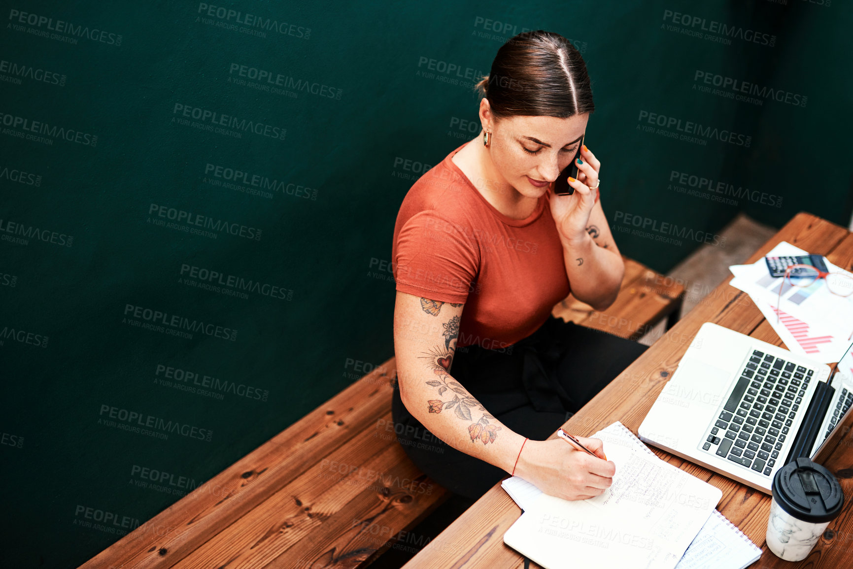 Buy stock photo Cropped shot of an attractive young businesswoman sitting alone and using her cellphone while writing in her notebook