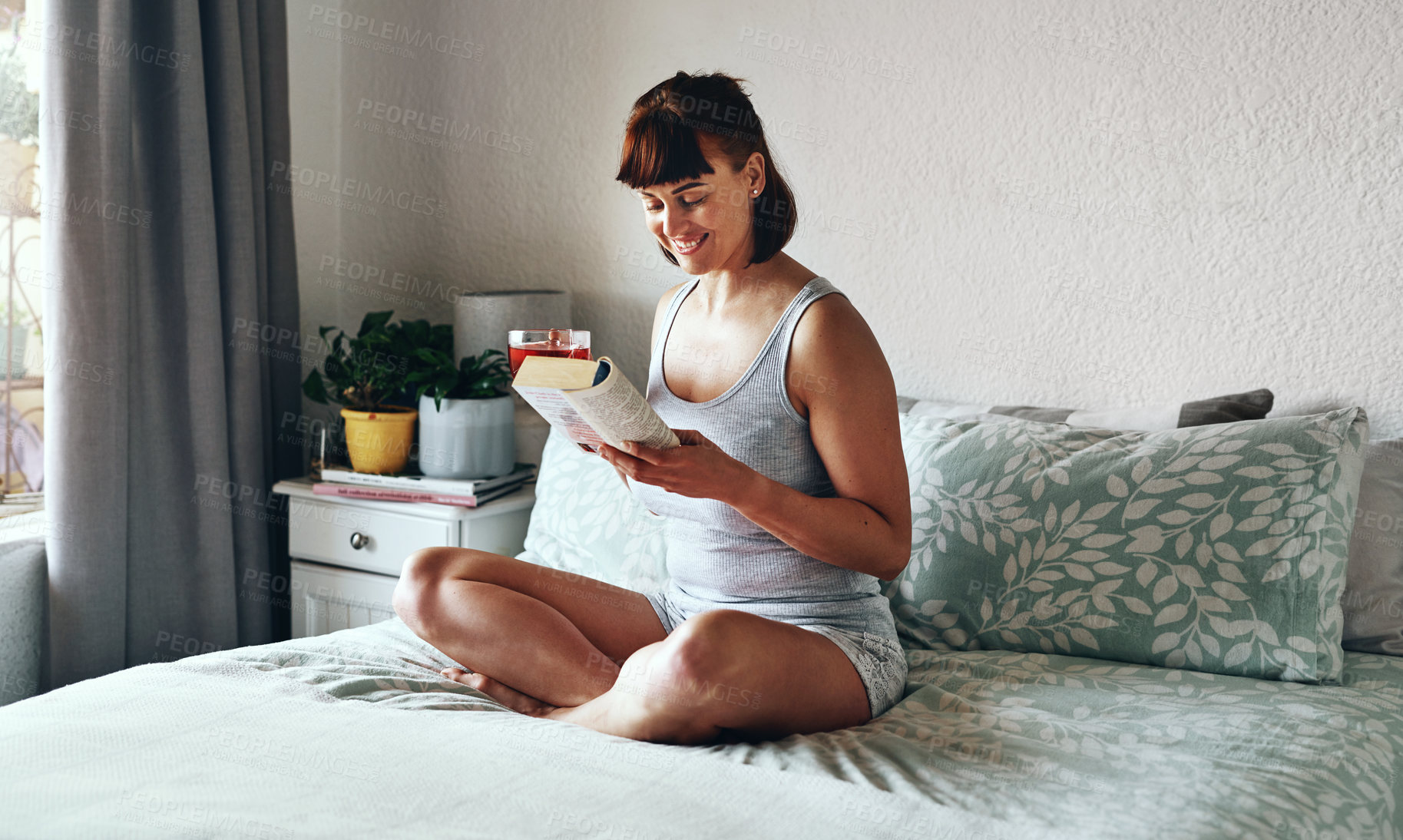 Buy stock photo Full length shot of an attractive young woman drinking tea and reading a book in her bedroom at home