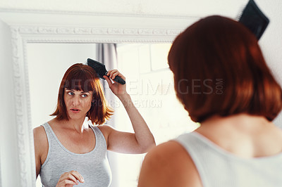 Buy stock photo Shot of an attractive young woman brushing her hair inside her bathroom at home