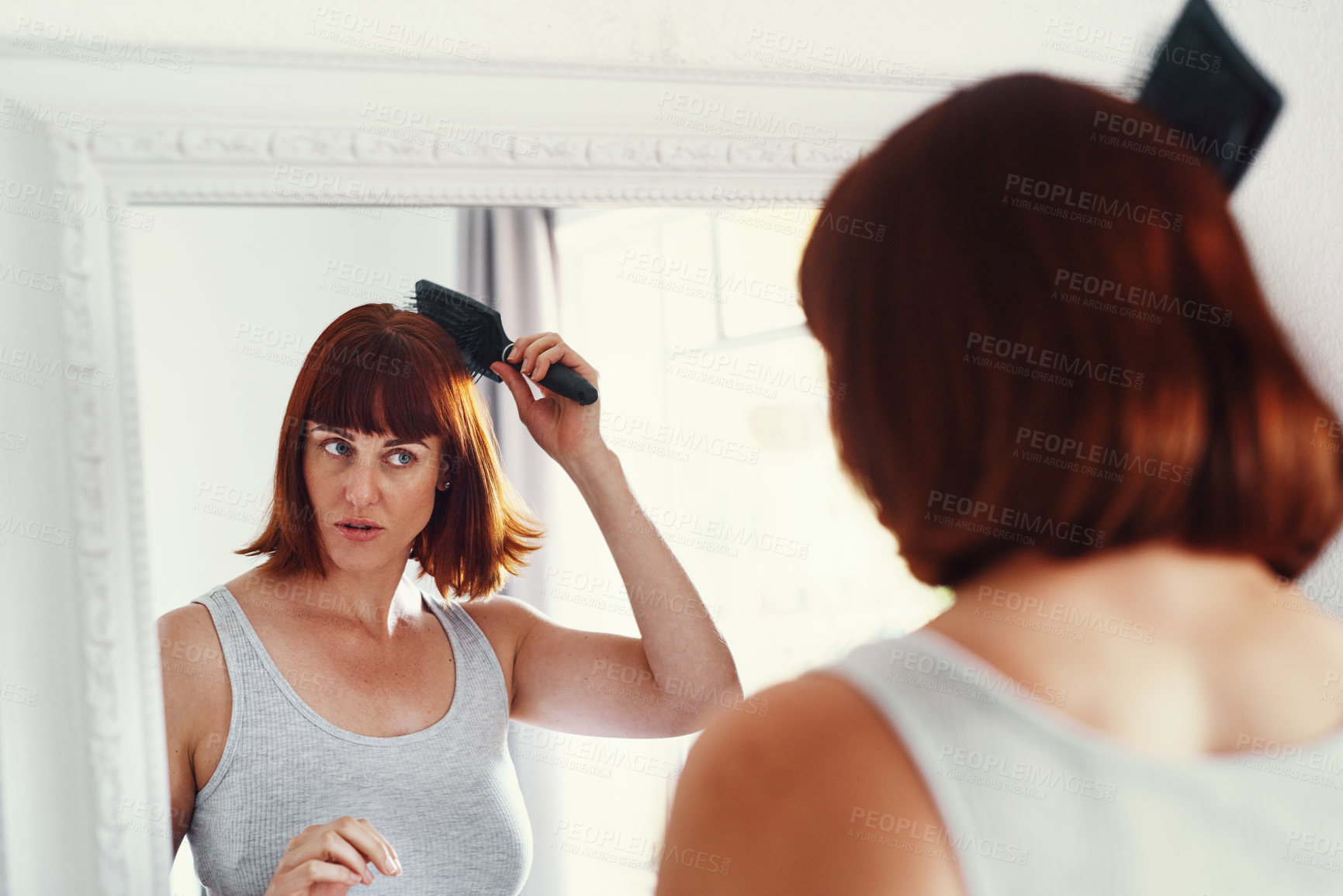 Buy stock photo Shot of an attractive young woman brushing her hair inside her bathroom at home