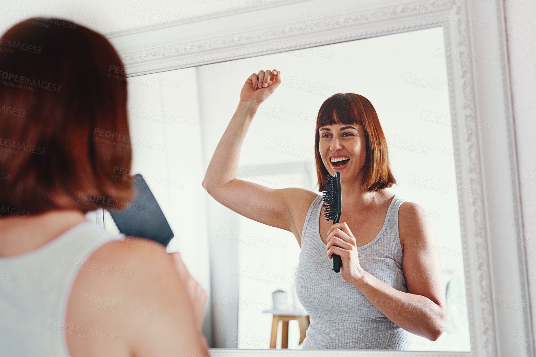 Buy stock photo Shot of an attractive young woman holding a hairbrush and singing in her bathroom at home