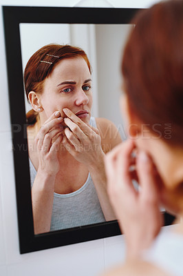 Buy stock photo Shot of an attractive young woman looking in the mirror and popping a pimple on her face at home