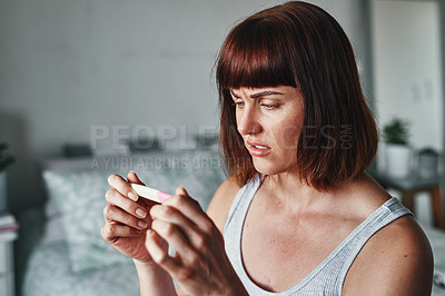 Buy stock photo Shot of an attractive young woman looking shocked while looking at her pregnancy test results at home
