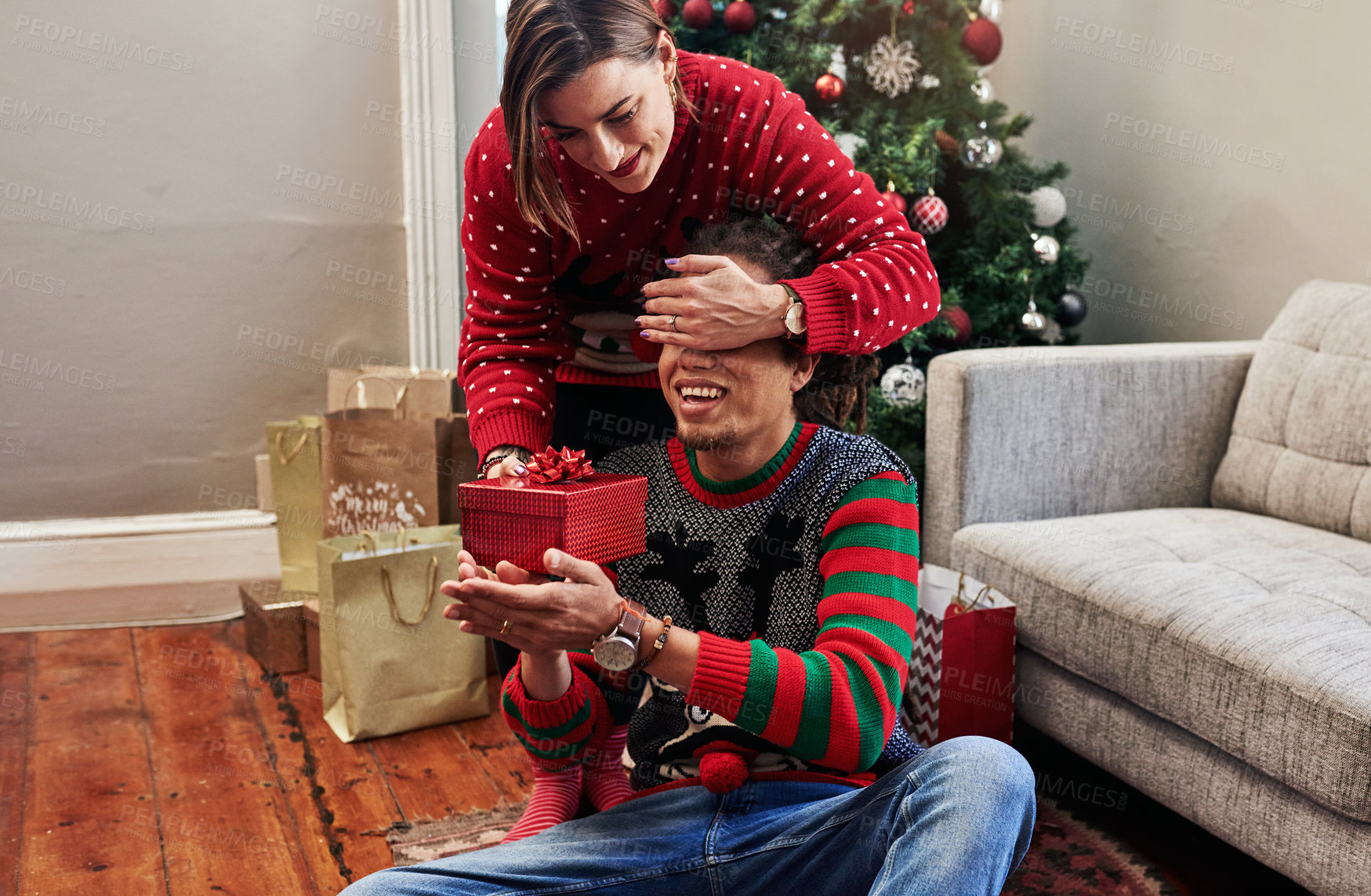 Buy stock photo Cropped shot of a cheerful young woman holding her husband's eyes closed while giving hime a present to open during christmas time at home
