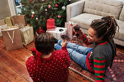 Buy stock photo High angle shot of a cheerful young couple enjoying a glass of wine together while being seated next to a christmas tree at home during the holiday season