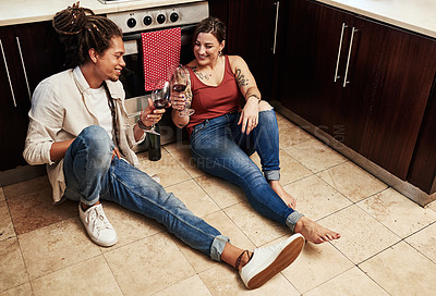 Buy stock photo Shot of a cheerful young couple enjoying a glass of wine together while being seated on the kitchen floor at home