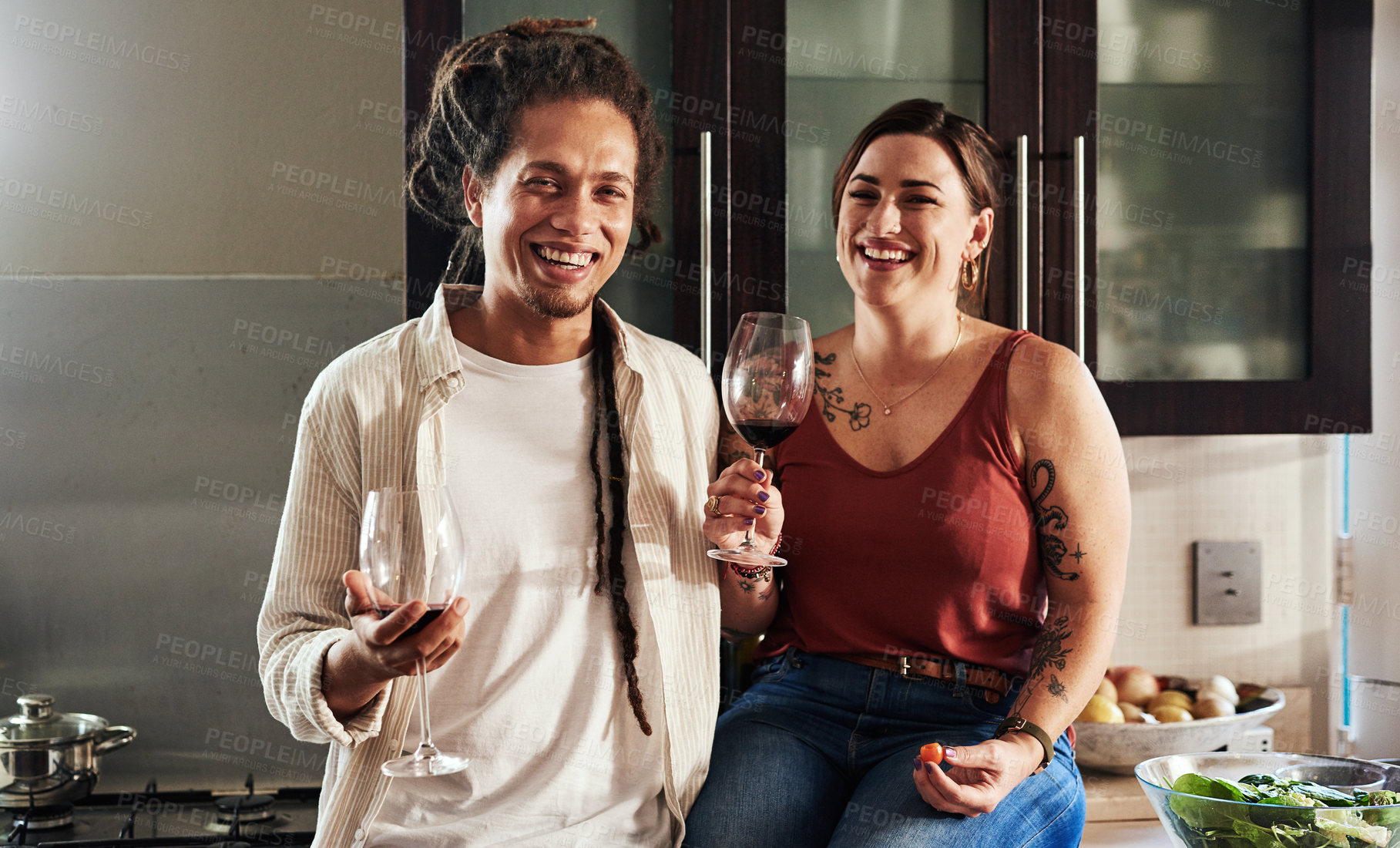 Buy stock photo Portrait of a cheerful young couple enjoying a glass of wine together while standing in the kitchen at home