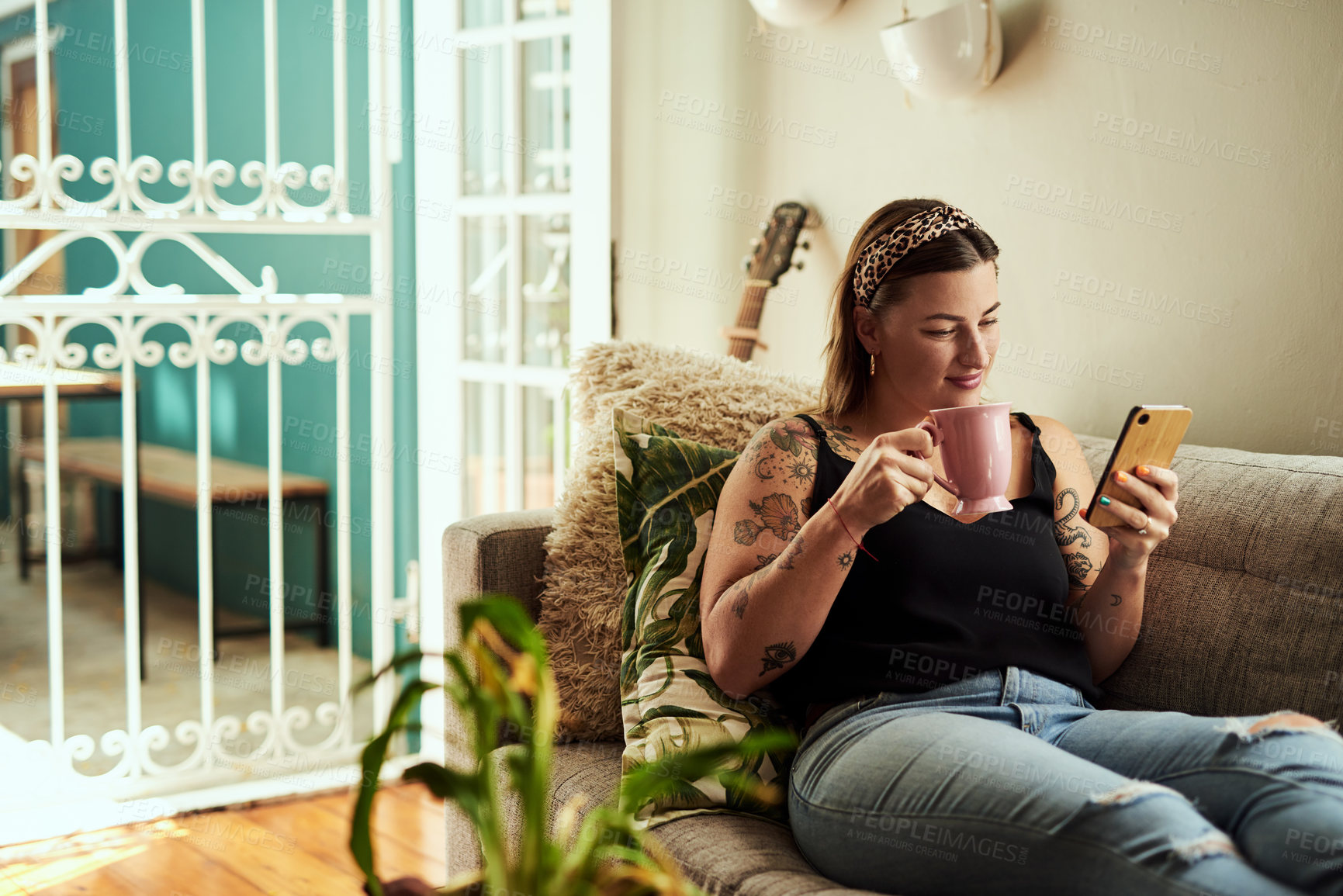 Buy stock photo Shot of a young woman having coffee and using a smartphone on the sofa at home