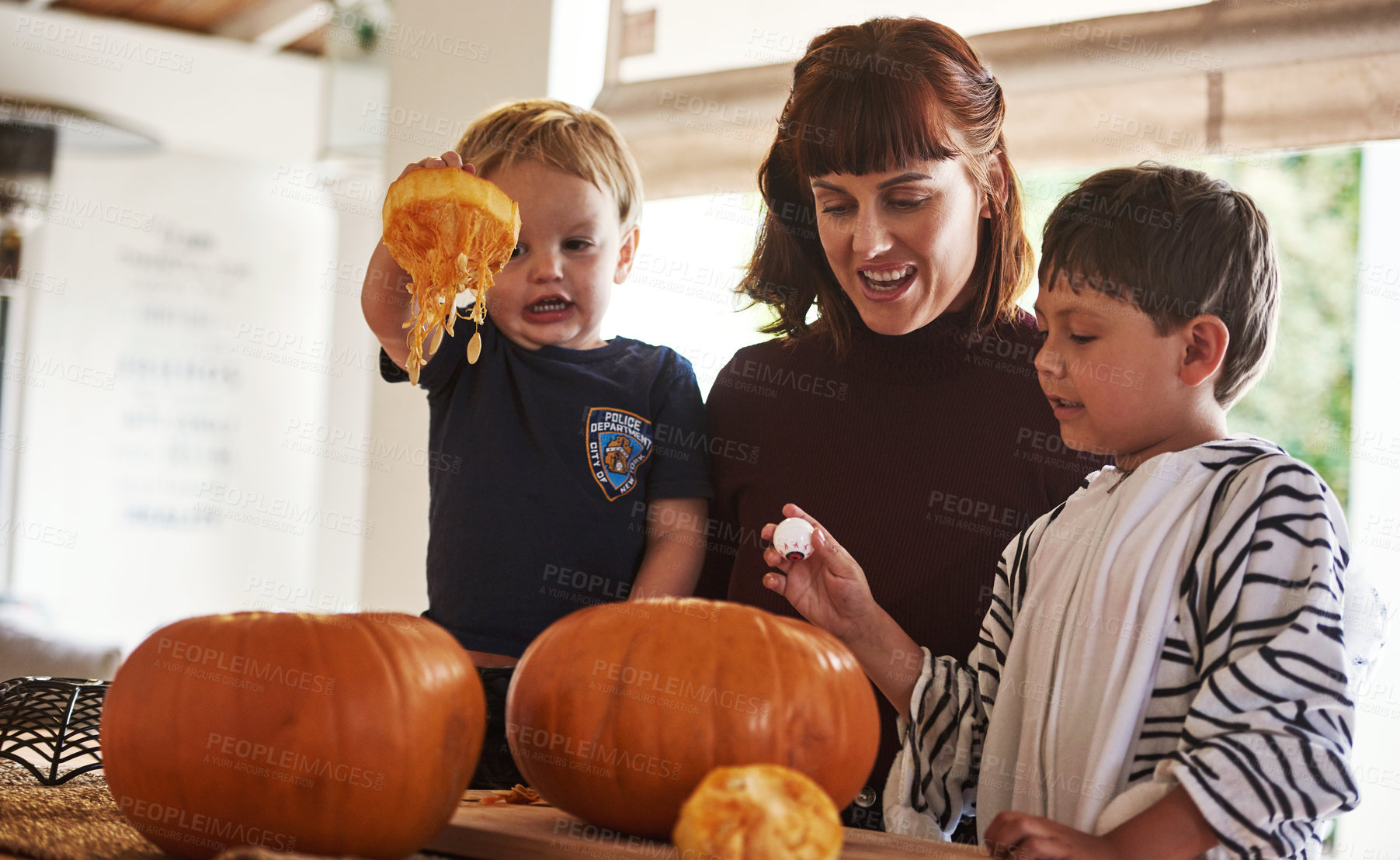 Buy stock photo Shot of two adorable little boys carving out pumpkins and celebrating halloween with their mother at home
