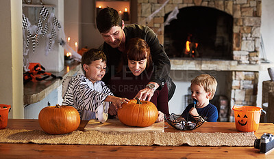 Buy stock photo Shot of an adorable young family carving out pumpkins and celebrating halloween together at home