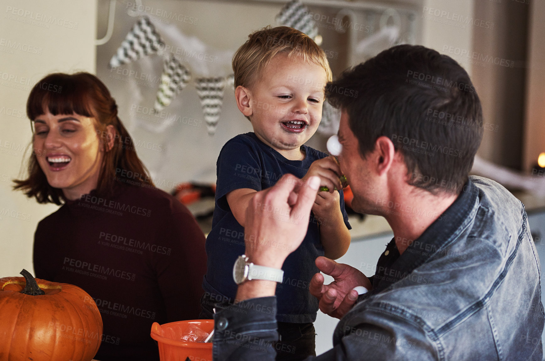 Buy stock photo Happy family, candy and kid with pumpkin for halloween to celebrate with love, support or smile. Dad, mom or parents with child eating sweets in vegetable for holiday, decoration and party in home