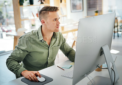 Buy stock photo Cropped shot of a handsome young businessman sitting and using his computer in the office