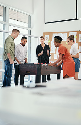 Buy stock photo Cropped shot of a diverse group of businesspeople standing together and bonding over a game of foosball in the office
