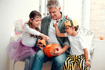 Buy stock photo Shot of two adorable young siblings carving out pumpkins for Halloween with their grandfather at home