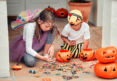 Buy stock photo Shot of two adorable young siblings looking at their Halloween candy at home