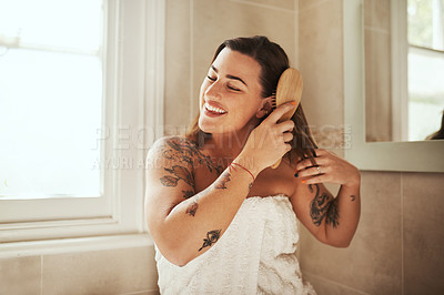 Buy stock photo Shot of an attractive young woman brushing her hair during her morning beauty routine at home