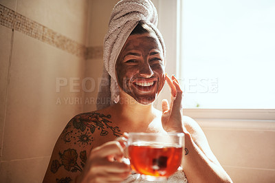 Buy stock photo Shot of a young woman having tea while giving herself a facial at home