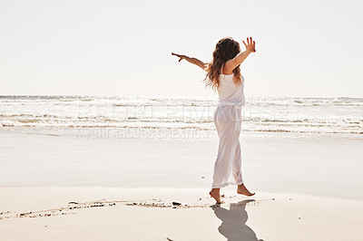 Buy stock photo Rearview shot of a young woman standing with her arms outstretched at the beach