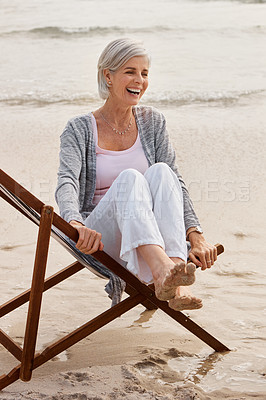 Buy stock photo Full length shot of an attractive middle aged woman sitting on a lounger at the beach