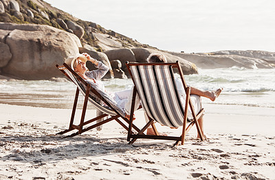 Buy stock photo Full length shot of an affectionate middle aged couple relaxing on loungers at the beach