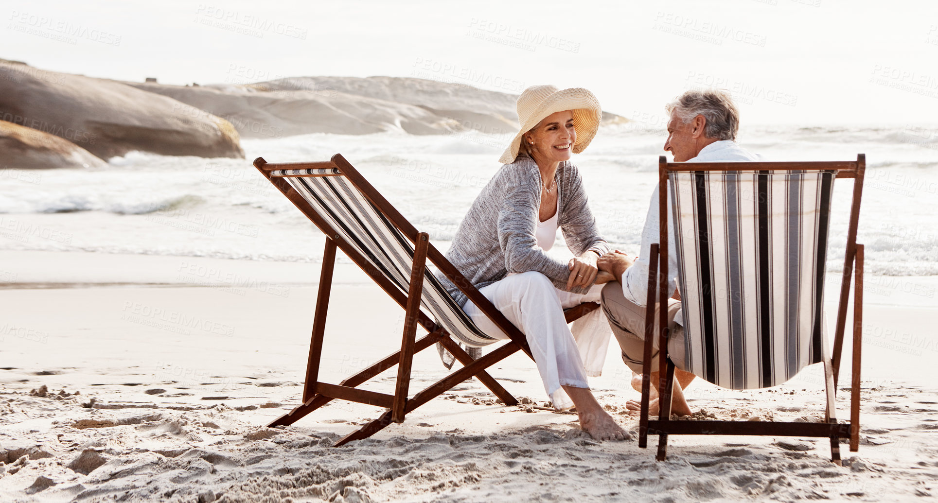 Buy stock photo Full length shot of an affectionate middle aged couple relaxing on loungers at the beach