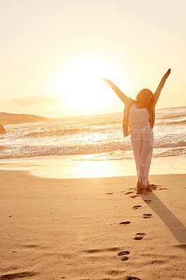 Buy stock photo Shot of a young woman standing with her arms outstretched at the beach