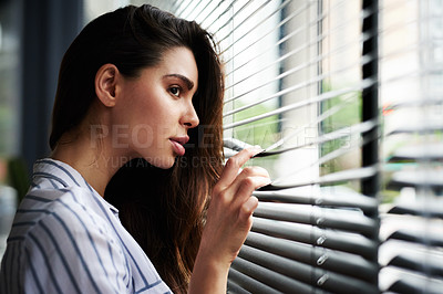 Buy stock photo Cropped shot of an attractive young woman looking through her window while standing indoors at home