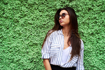 Buy stock photo Cropped shot of an attractive young woman looking away while standing against a green wall during the day