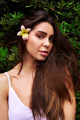 Buy stock photo Cropped portrait of an attractive young woman standing outdoors while wearing a flower on her hair during the day