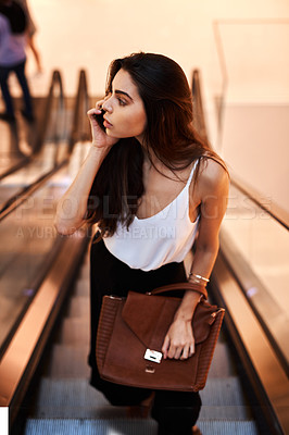 Buy stock photo Cropped shot of an attractive young woman taking a phonecall while standing on an escalator during the day