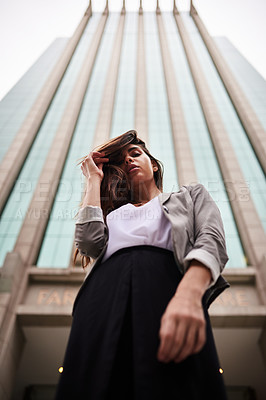 Buy stock photo Low angle portrait of an attractive young woman standing outdoors in the city