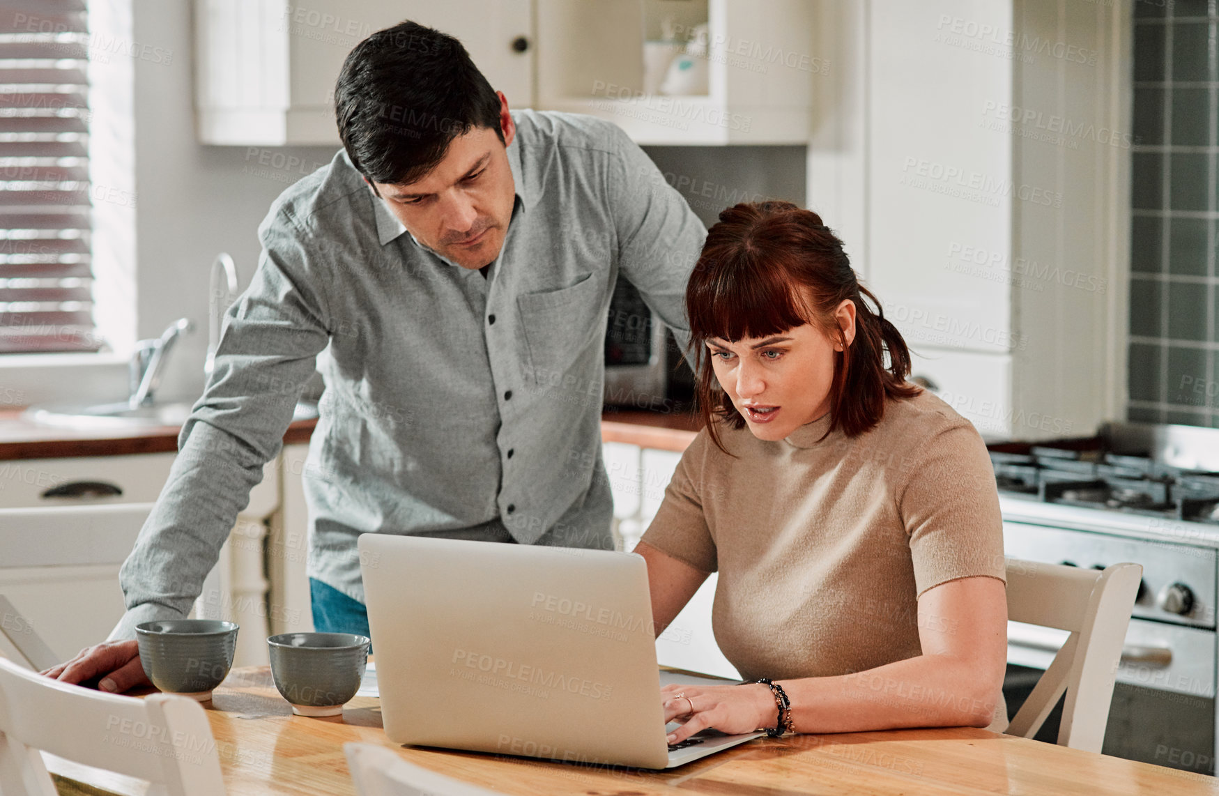 Buy stock photo Shot of a woman using a laptop with her husband standing beside her
