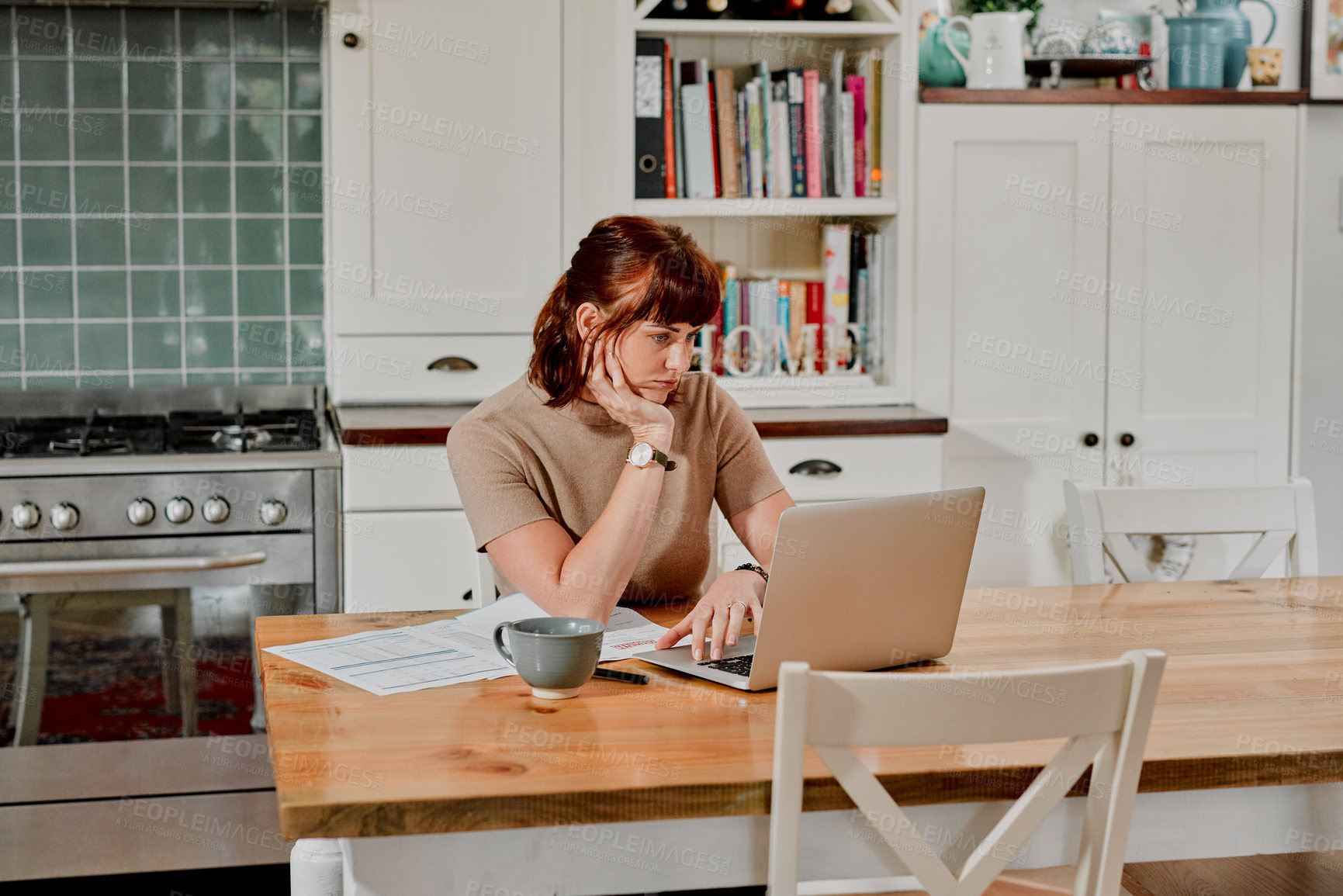 Buy stock photo Shot of a woman sitting at home with paperwork and her laptop