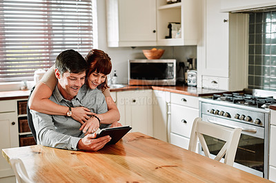 Buy stock photo Shot of a man using a digital tablet while being embraced by his wife at home