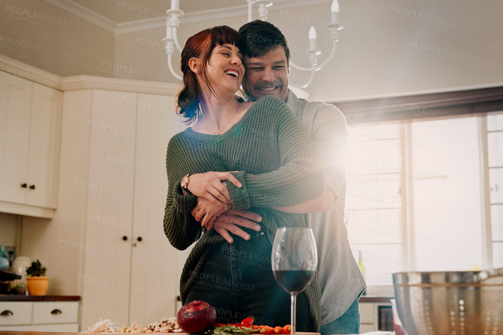 Buy stock photo Shot of a woman cooking while being embraced by her husband at home