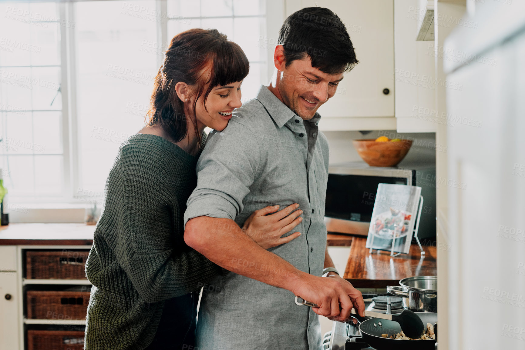 Buy stock photo Shot of a man cooking while being embraced by his wife at home