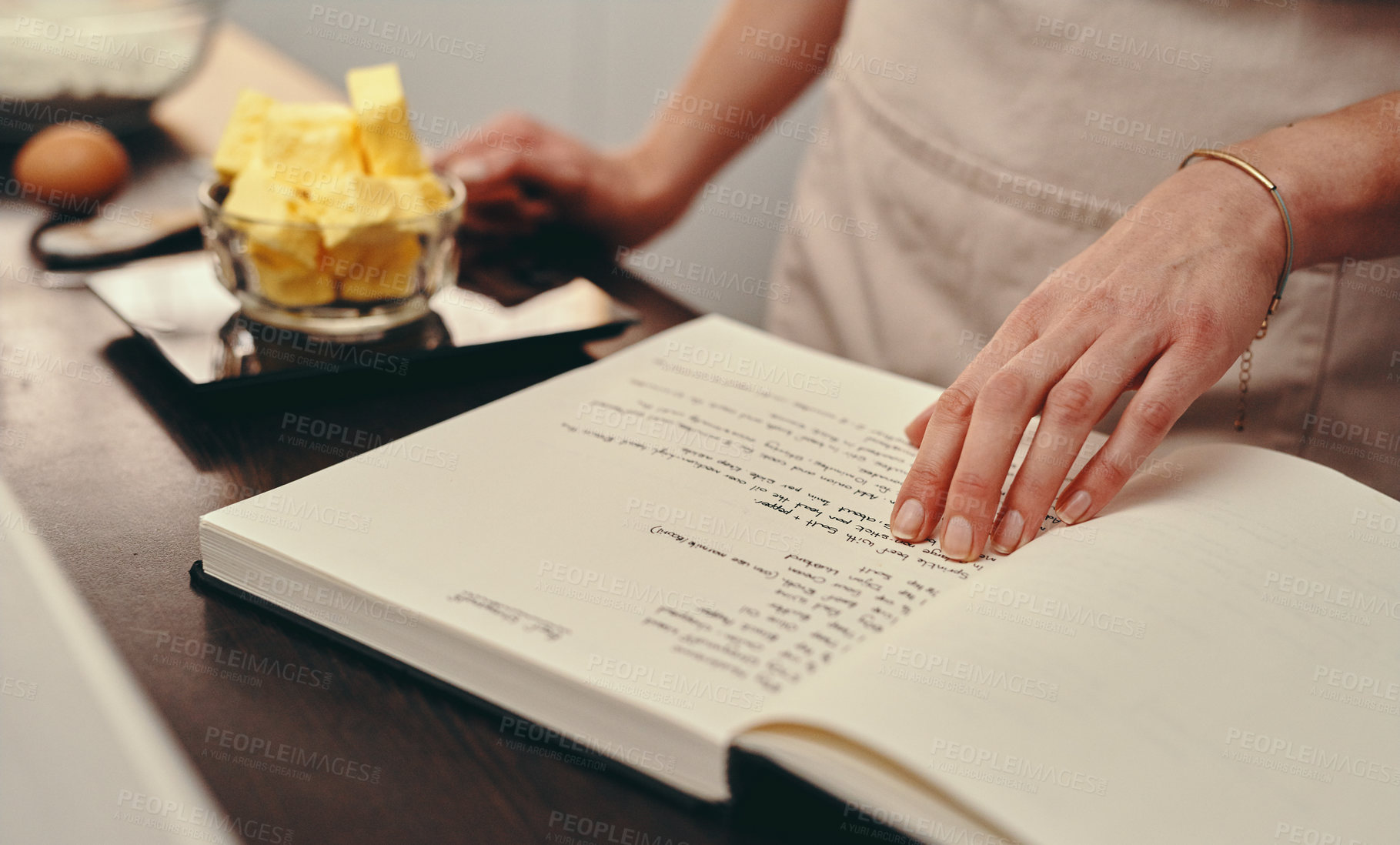 Buy stock photo Cropped shot of an unrecognizable woman reading a recipe from a book while baking at home
