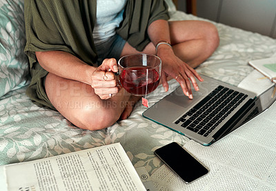 Buy stock photo Cropped shot of an unrecognizable woman drinking tea and using a laptop while relaxing in her bedroom at home