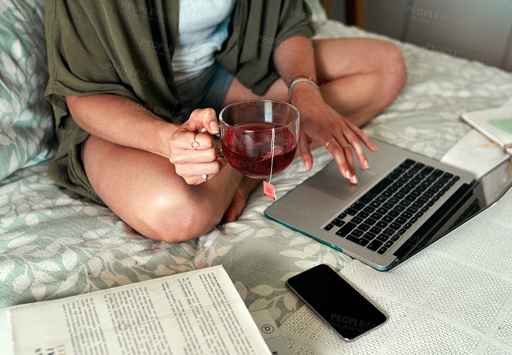 Buy stock photo Cropped shot of an unrecognizable woman drinking tea and using a laptop while relaxing in her bedroom at home