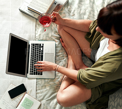 Buy stock photo High angle shot of a young woman drinking tea and using a laptop while relaxing in her bedroom at home